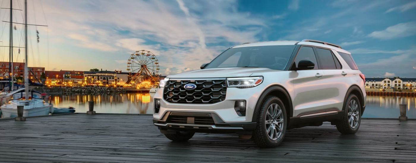 A silver 2026 Ford Explorer® SUV parked on a pier near an amusement park.