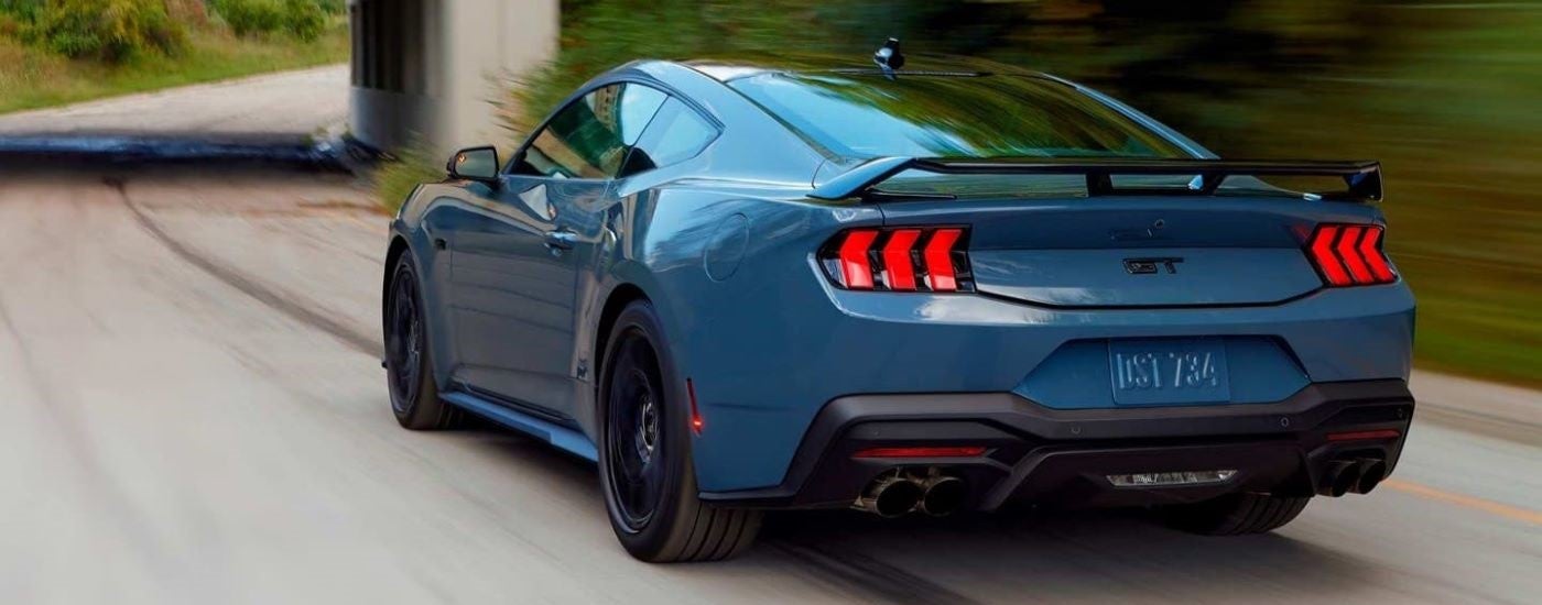 Rear of a blue 2024 Ford Mustang GT driving down a road.