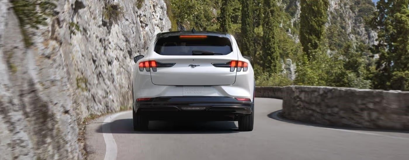 Rear of a white 2023 Ford Mustang Mach-E driving on a mountainous road